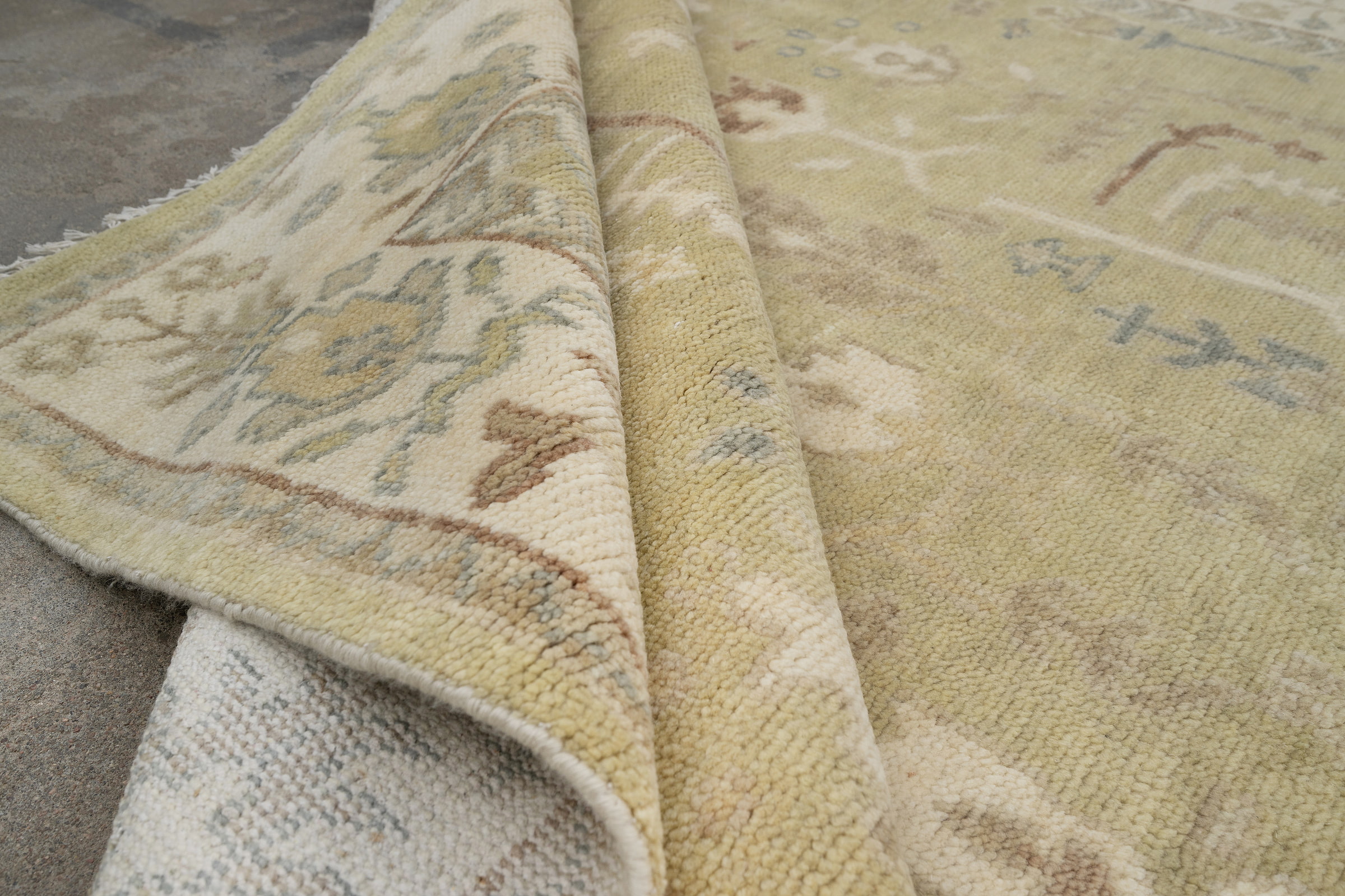 Hand-knotted wool Oushak rug with a sage-green field, ivory multi-band border, and scattered botanical palmette and tree motifs in soft rust, cream, and slate tones.
