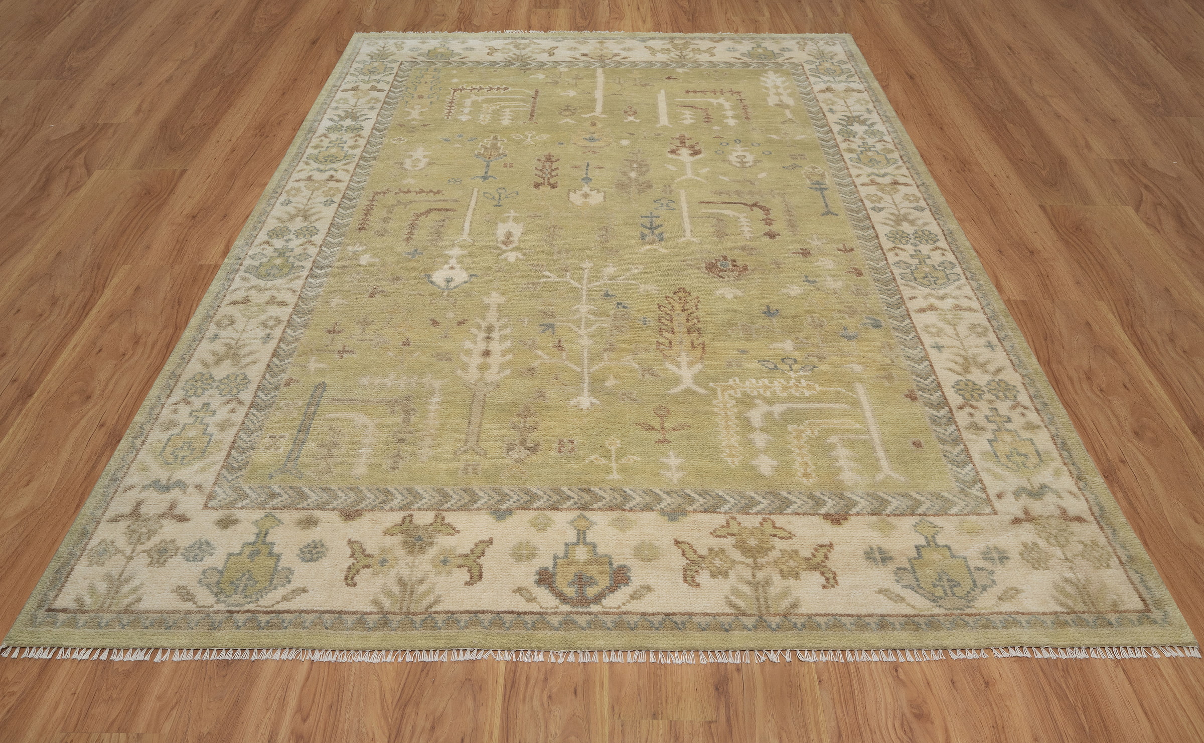 Hand-knotted wool Oushak rug with a sage-green field, ivory multi-band border, and scattered botanical palmette and tree motifs in soft rust, cream, and slate tones.