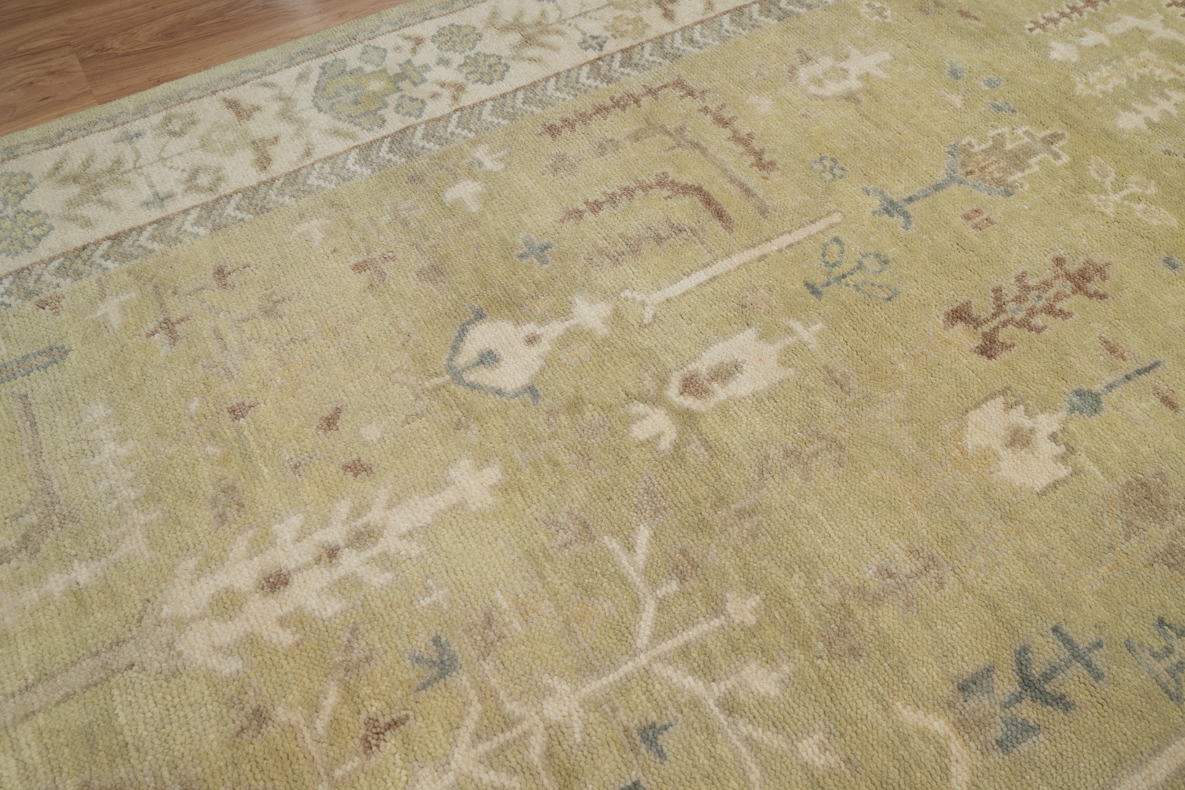 Hand-knotted wool Oushak rug with a sage-green field, ivory multi-band border, and scattered botanical palmette and tree motifs in soft rust, cream, and slate tones.