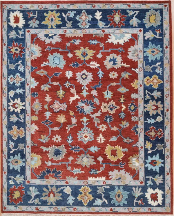 Hand-knotted wool Oushak rug with a rust field, wide navy border, and allover palmette, rosette, vine, and serrated-leaf motifs in ivory, gold, blue, and sage.