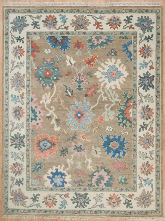 Hand-knotted wool Oushak rug with a beige field, wide ivory border, and oversized rosette, palmette, vine, and serrated-leaf motifs in teal, coral, blush, and navy.
