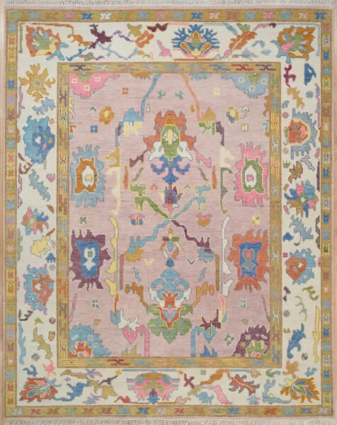 Hand-knotted wool Oushak rug with a blush field, multi-band ivory and gold border, and oversized palmette, rosette, vine, serrated-leaf, and scroll motifs in rust, blue, olive, burgundy, and teal.