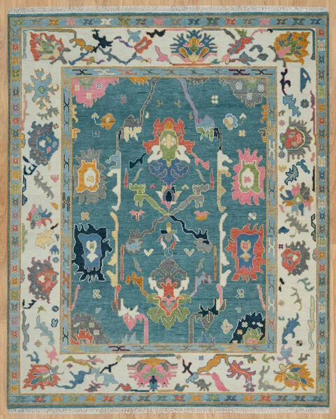 Hand-knotted wool Oushak rug with a teal field, wide ivory border, and oversized palmette, rosette, vine, and serrated-leaf motifs in blush, coral, navy, rust, olive, and gold.