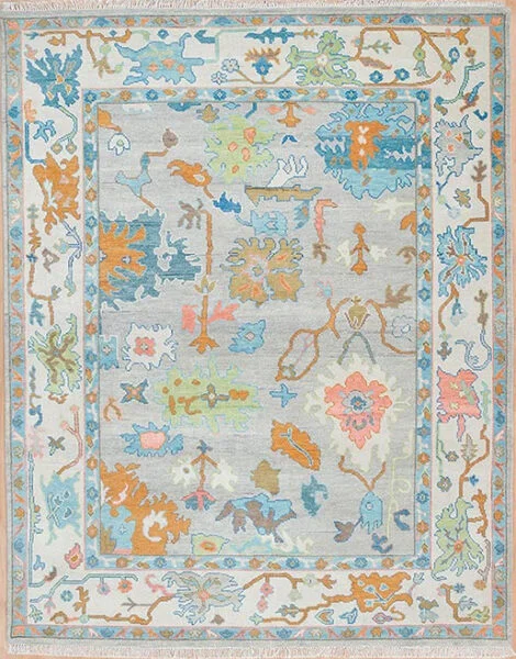 Hand-knotted wool oushak rug with a light grey field, wide ivory border, and loosely spaced palmettes and rosettes in amber, blue, and coral with a pale, understated palette.