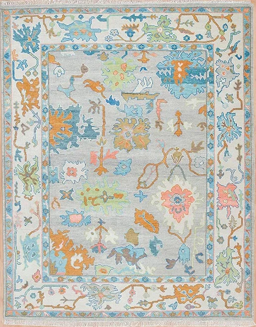 Hand-knotted wool oushak rug with a light grey field, wide ivory border, and loosely spaced palmettes and rosettes in amber, blue, and coral with a pale, understated palette.