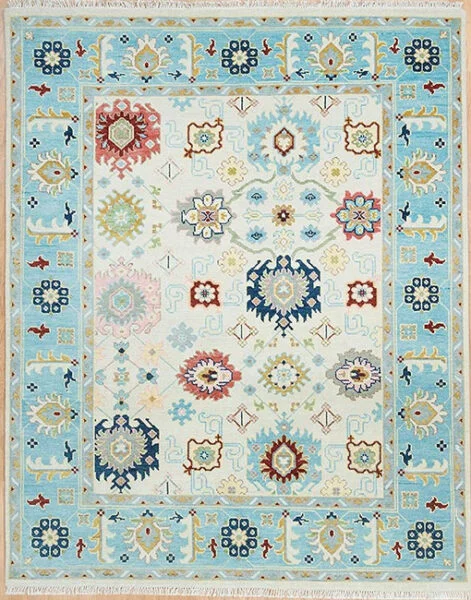 Hand-knotted wool oushak rug with an ivory field, wide aqua border, and rhythmically placed rosettes and palmettes in navy, burgundy, and gold with crisp figure-ground contrast.