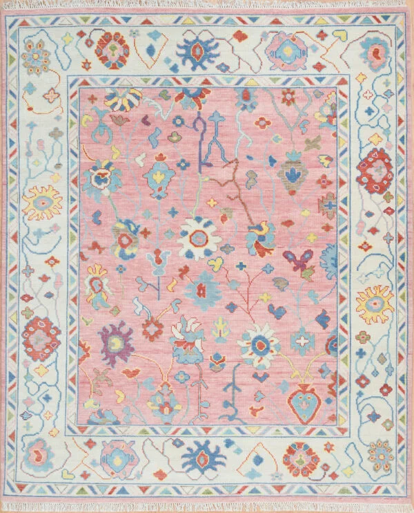 Hand-knotted wool oushak rug with a pale rose field, multi-band ivory border, and airy scattered small rosettes and tulips in blue and coral with generous open pink ground.