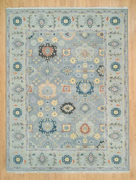 Hand-knotted wool oushak rug with a grey-blue field, narrow grey border, and densely packed small rosettes, palmettes, and diamond motifs in gold, navy, and coral.