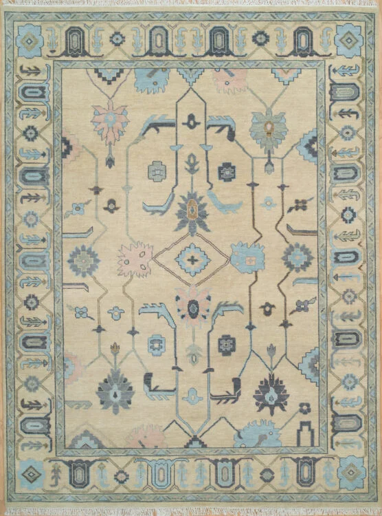 Hand-knotted wool oushak rug with a warm sand field, wide teal-grey border, and geometric palmette, angular-vine, diamond, and tulip motifs in muted navy and blue with structured, traditional character.