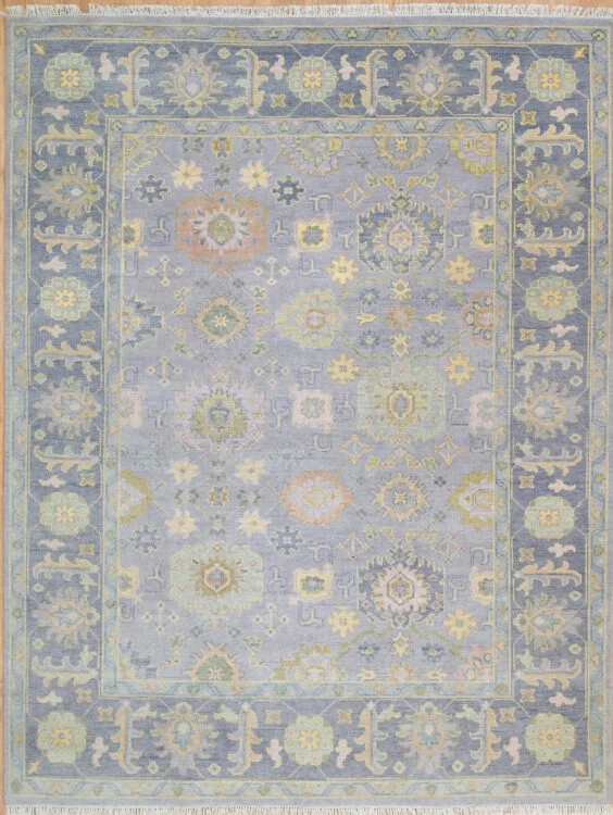 Hand-knotted wool oushak rug with a soft slate field, wide slate border, and dense small-scale rosettes and palmettes in muted gold, sage, blush, and mauve.