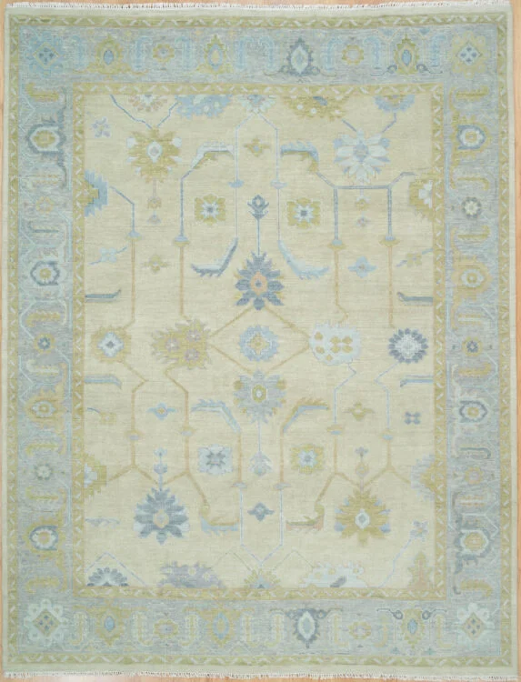 Hand-knotted wool oushak rug with a warm sand field, wide blue border, and calm balanced palmettes and rosettes in muted blue and olive with subtle figure-ground contrast.