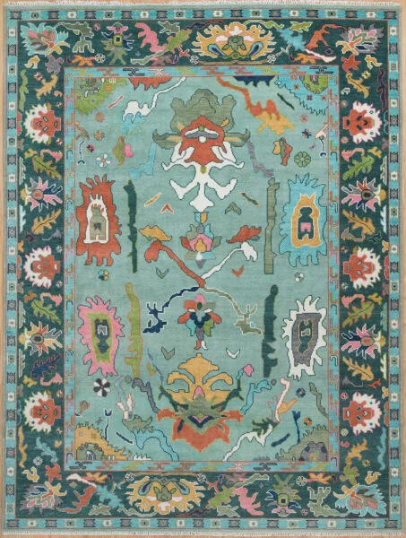 Hand-knotted wool oushak rug with a rich teal field, wide dark charcoal border, and dense oversized vivid palmettes, rosettes, and scrolls in coral, ivory, green, and rose.