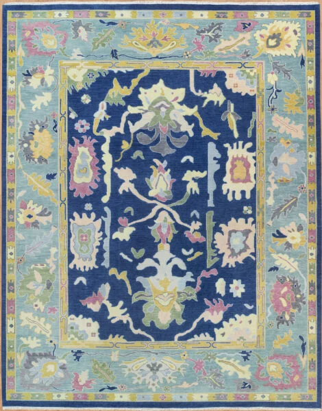Hand-knotted wool oushak rug with a deep navy field, wide light blue border, and dense oversized palmettes and rosettes in pastel ivory, rose, and green with bold glowing contrast.