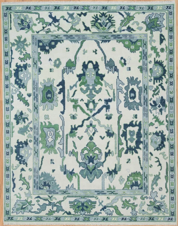Hand-knotted wool oushak rug with a bright ivory field, wide green border, and dense oversized bold palmettes and rosettes in green, navy, and teal with minimal open ground.