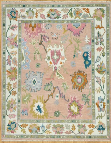 Hand-knotted wool Oushak rug with a peach field featuring oversized palmettes in pink, blue, olive, and coral, framed by a wide ivory vine border.