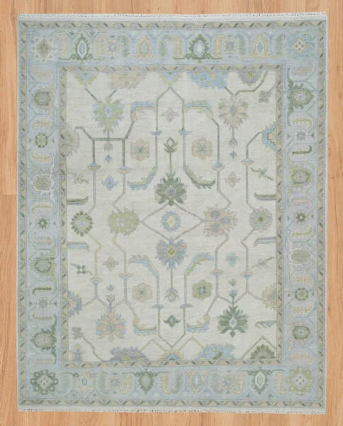 Hand-knotted wool Oushak rug with a cream field featuring palmettes and serrated leaves in sage, olive, and soft blue, framed by a wide blue multi-band geometric border.