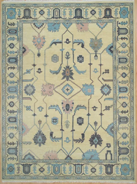 Hand-knotted wool Oushak rug with a sand field featuring angular vines and palmettes in charcoal and blue, framed by a wide pale blue geometric scroll border.