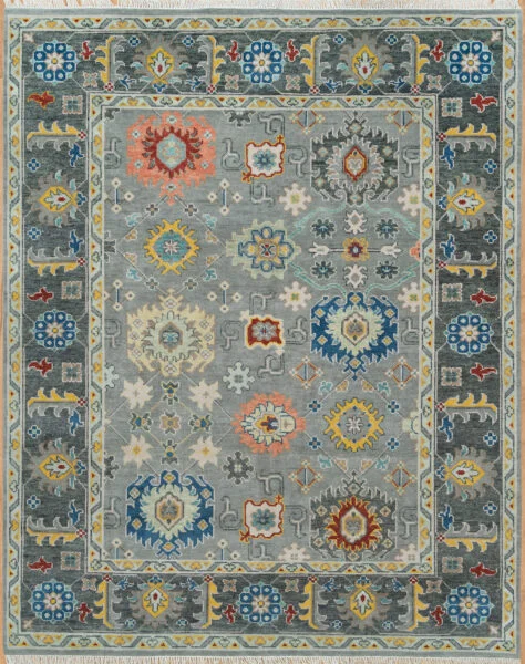 Hand-knotted wool Oushak rug with a steel-grey field featuring densely arranged palmettes and rosettes in blue, gold, rust, and coral, framed by a wide charcoal serrated-leaf border.