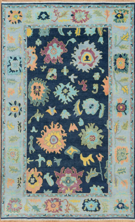 Hand-knotted wool Oushak rug with deep navy field, pale blue border, and large-scale floral palmettes in peach, aqua, gold, and green.