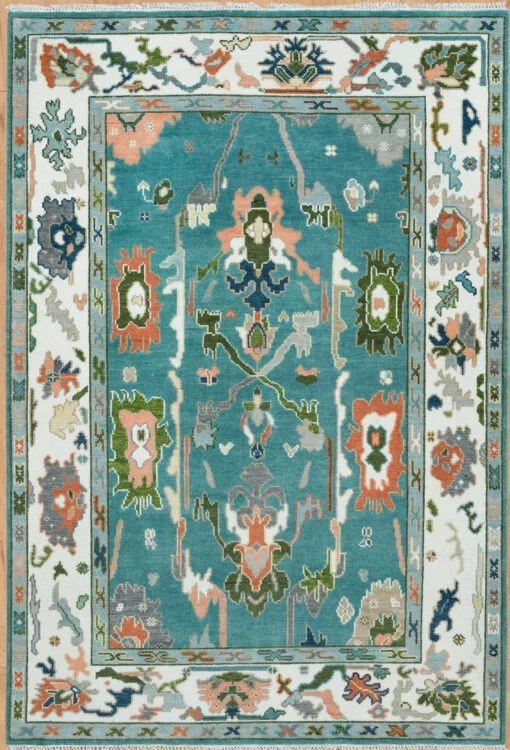 Hand-knotted wool Oushak rug with teal field, ivory border, and large floral palmettes in peach, green, navy, and grey.