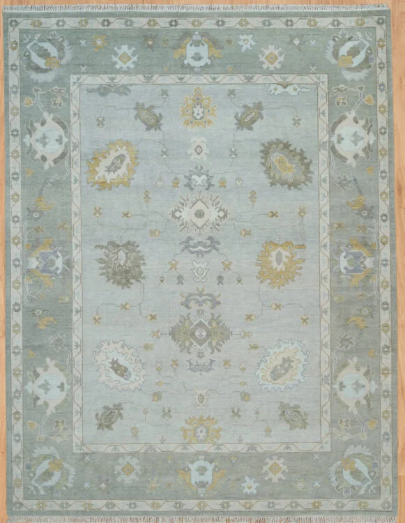 Hand-knotted wool Oushak rug with sage field, tonal border, and muted floral palmettes in gold, grey, and blue.