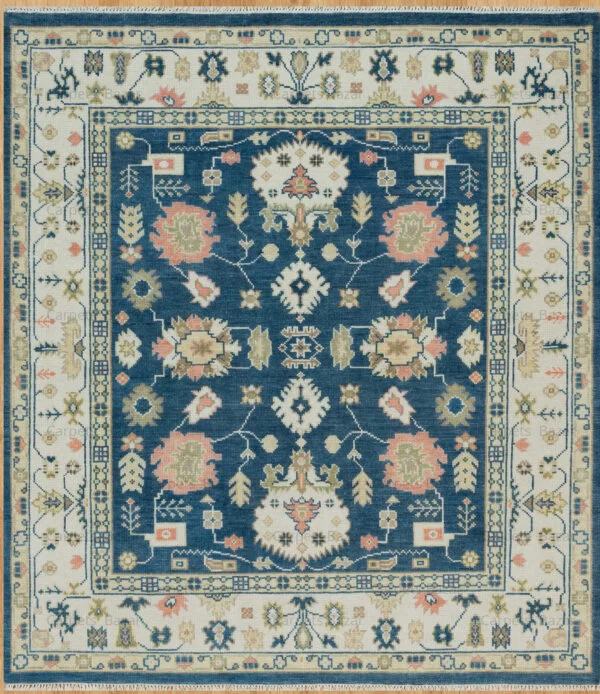Hand-knotted wool Oushak rug with deep navy field, ivory border, and floral palmettes in ivory, peach, gold, and green.