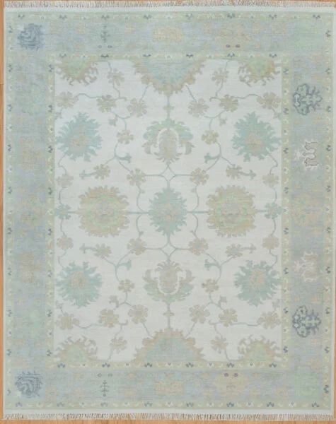 Hand-knotted wool Oushak rug with very light ivory field, pale blue border, and soft floral palmettes in sage, teal, and gold.