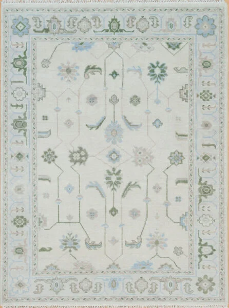 Hand-knotted wool Oushak rug with ivory field, pale blue border, and symmetrical floral palmettes in green, blue, and sage.
