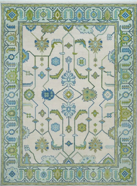 Hand-knotted modern Oushak wool rug with an ivory field, blue rosettes and sage-green vine stems, framed by a structured blue-green geometric border.