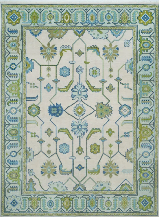 Hand-knotted modern Oushak wool rug with an ivory field, blue rosettes and sage-green vine stems, framed by a structured blue-green geometric border.