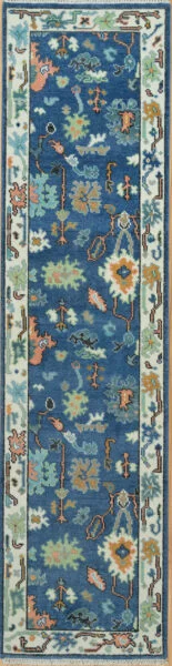 Hand-knotted modern Oushak wool runner with a saturated blue field, dense aqua, coral and green floral motifs, and a narrow ivory border.