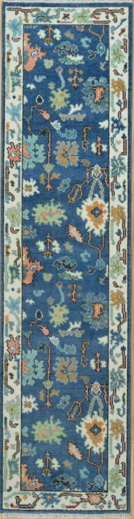 Hand-knotted modern Oushak wool runner with a saturated blue field, dense aqua, coral and green floral motifs, and a narrow ivory border.
