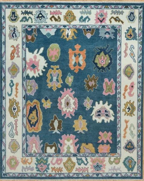 Hand-knotted modern Oushak wool rug with a mid-blue field, oversized abstract palmettes in coral, green, gold and pink, and an ivory floral border.