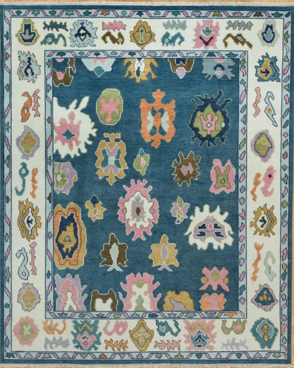 Hand-knotted modern Oushak wool rug with a mid-blue field, oversized abstract palmettes in coral, green, gold and pink, and an ivory floral border.