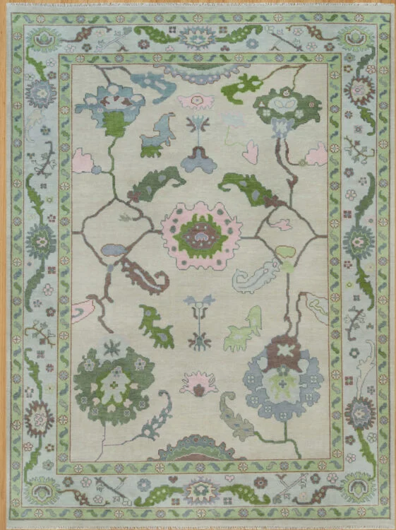 Hand-knotted wool oushak rug with a pale sage field, wide green border, and open large-scale palmettes, rosettes, and cloud-bands in green, blush, blue, and brown.