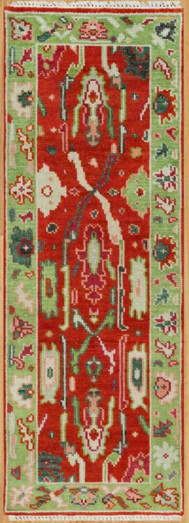 Hand-knotted wool oushak runner with a vivid red field, wide green border, and dense large-scale palmettes and rosettes in green, ivory, teal, and blush.