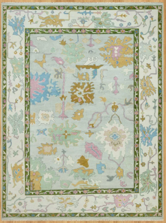 Hand-knotted wool oushak rug with a pale sage field, wide ivory border, and scattered large-scale palmettes and rosettes in blue, gold, blush, and olive.