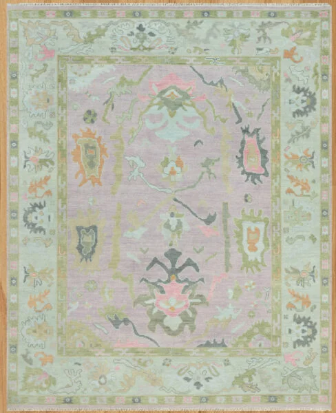 Hand-knotted wool oushak rug with a soft mauve field, wide sage border, and open large-scale palmettes and rosettes in sage, olive, coral, and charcoal.