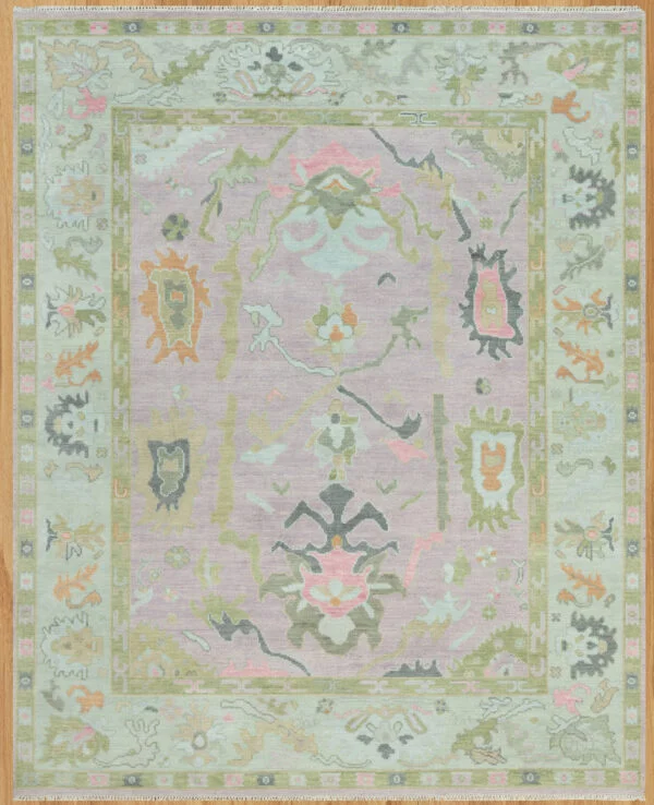 Hand-knotted wool oushak rug with a soft mauve field, wide sage border, and open large-scale palmettes and rosettes in sage, olive, coral, and charcoal.