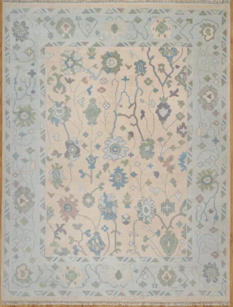 Hand-knotted wool oushak rug with a warm beige field, wide ivory-green border, and balanced medium-scale palmettes and rosettes in blue, sage, rust, and plum.