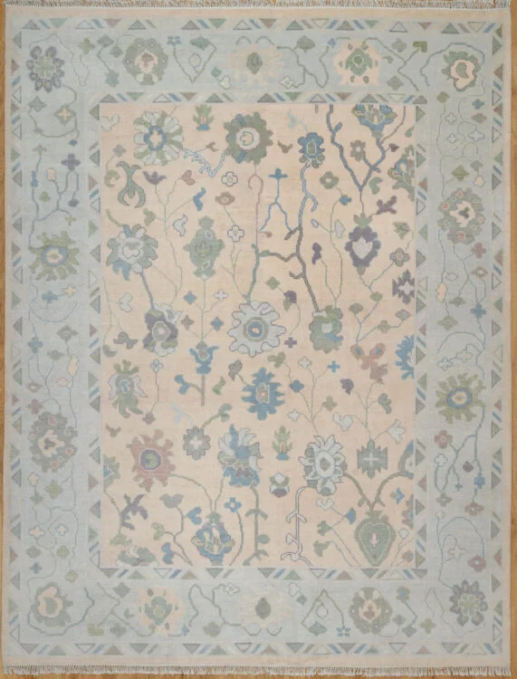 Hand-knotted wool oushak rug with a warm beige field, wide ivory-green border, and balanced medium-scale palmettes and rosettes in blue, sage, rust, and plum.