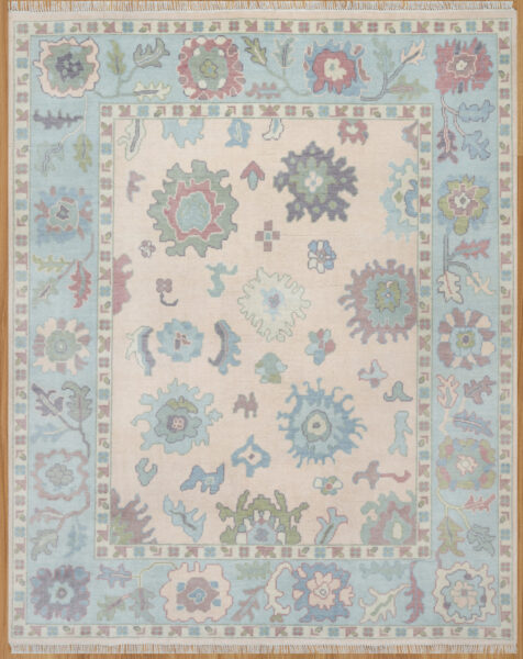 Hand-knotted wool oushak rug (8x10) with a pale blush field, wide blue border, and open large-scale palmettes and rosettes in blue, sage, rust, and plum.