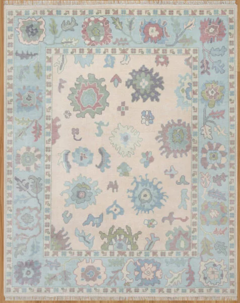 Hand-knotted wool oushak rug (8x10) with a pale blush field, wide blue border, and open large-scale palmettes and rosettes in blue, sage, rust, and plum.