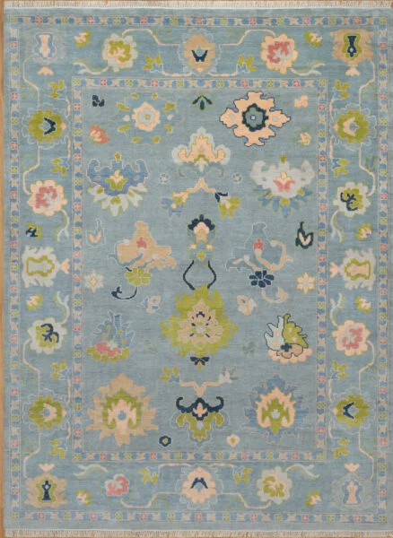 Hand-knotted wool oushak rug with a soft blue field, wide blue border, and balanced large-scale palmettes and rosettes in olive, blush, navy, and peach.