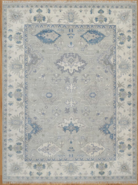 Hand-knotted wool oushak rug with a light grey field, wide ivory border, and balanced large-scale palmettes and rosettes in blue, ivory, blush, and navy.