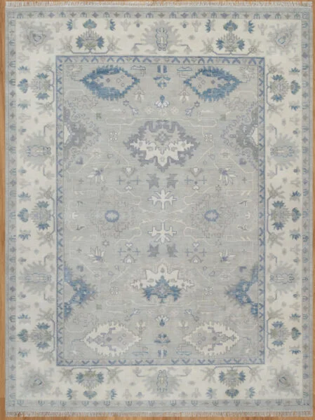 Hand-knotted wool oushak rug with a light grey field, wide ivory border, and balanced large-scale palmettes and rosettes in blue, ivory, blush, and navy.